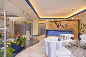 Eine moderne Hotelhalle mit Empfangstresen, Sitzgelegenheiten und einer Glastrennwand.