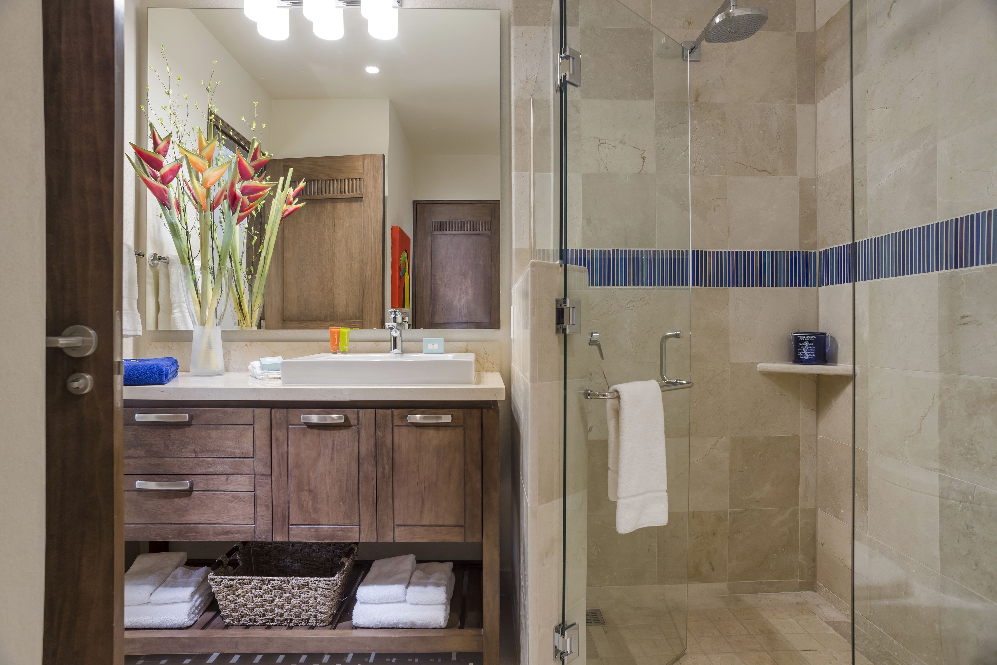 A modern bathroom with a shower, a sink with a mirror, and a vanity with drawers and a basket.