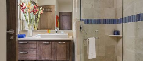 A modern bathroom with a shower, a sink with a mirror, and a vanity with drawers and a basket.