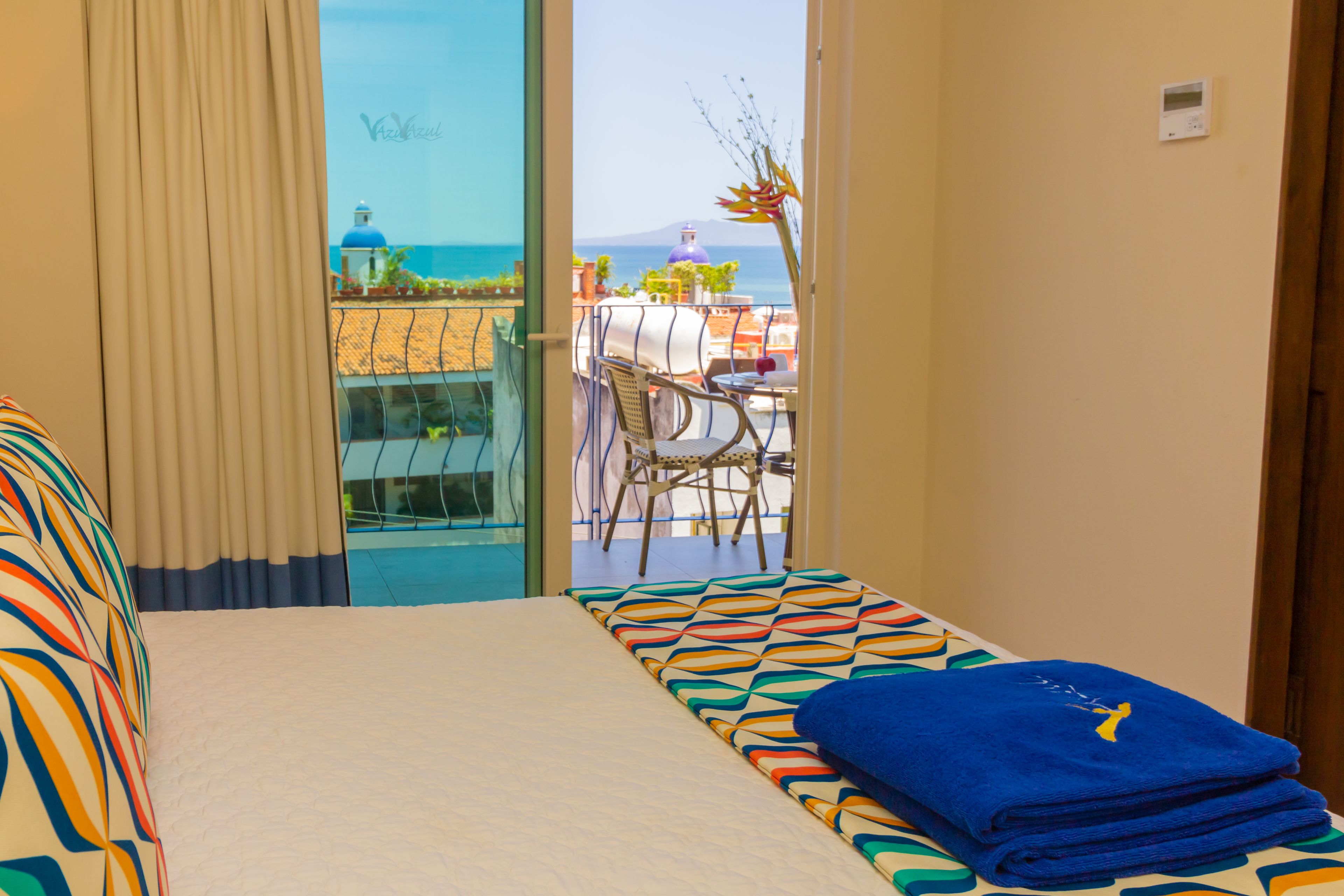Une chambre d’hôtel avec un lit, une vue sur la mer et un balcon équipé d’une table et de chaises.
