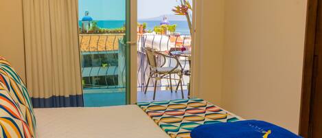 Une chambre d’hôtel avec un lit, une vue sur la mer et un balcon équipé d’une table et de chaises.