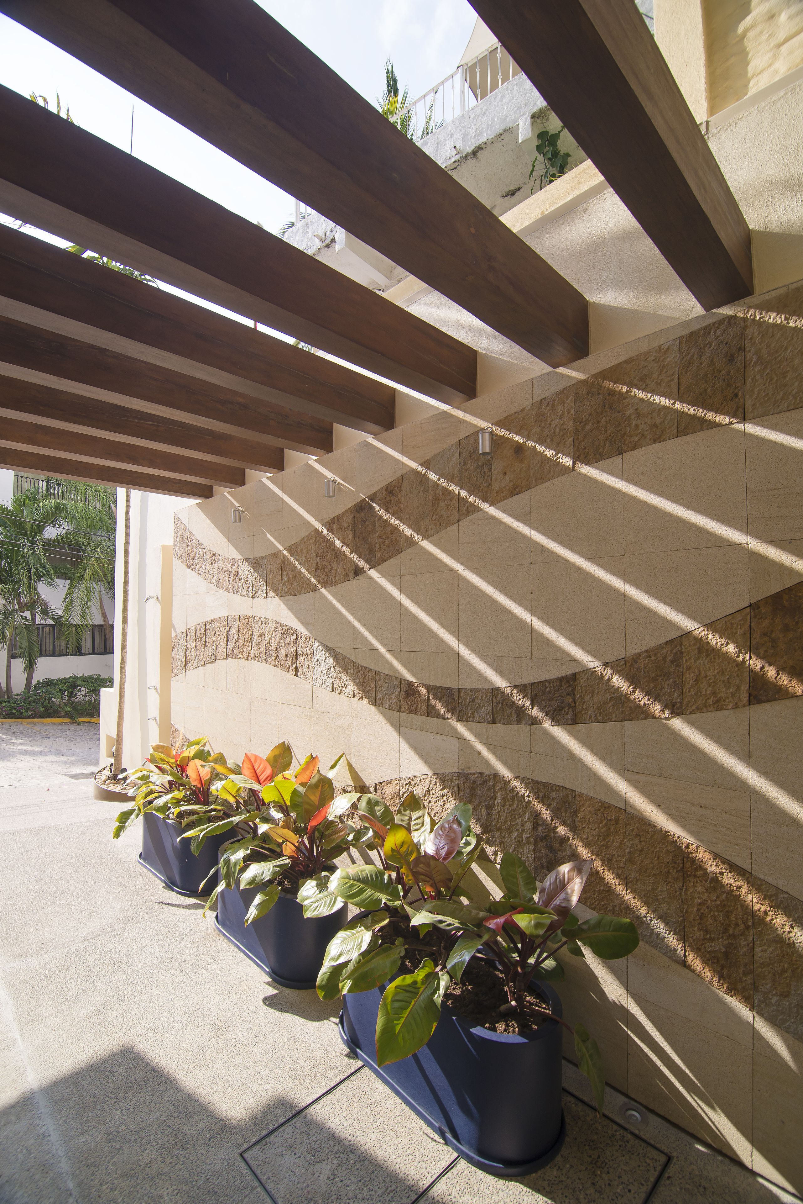 A covered outdoor area with wooden beams and potted plants against a wall with a stone pattern.
