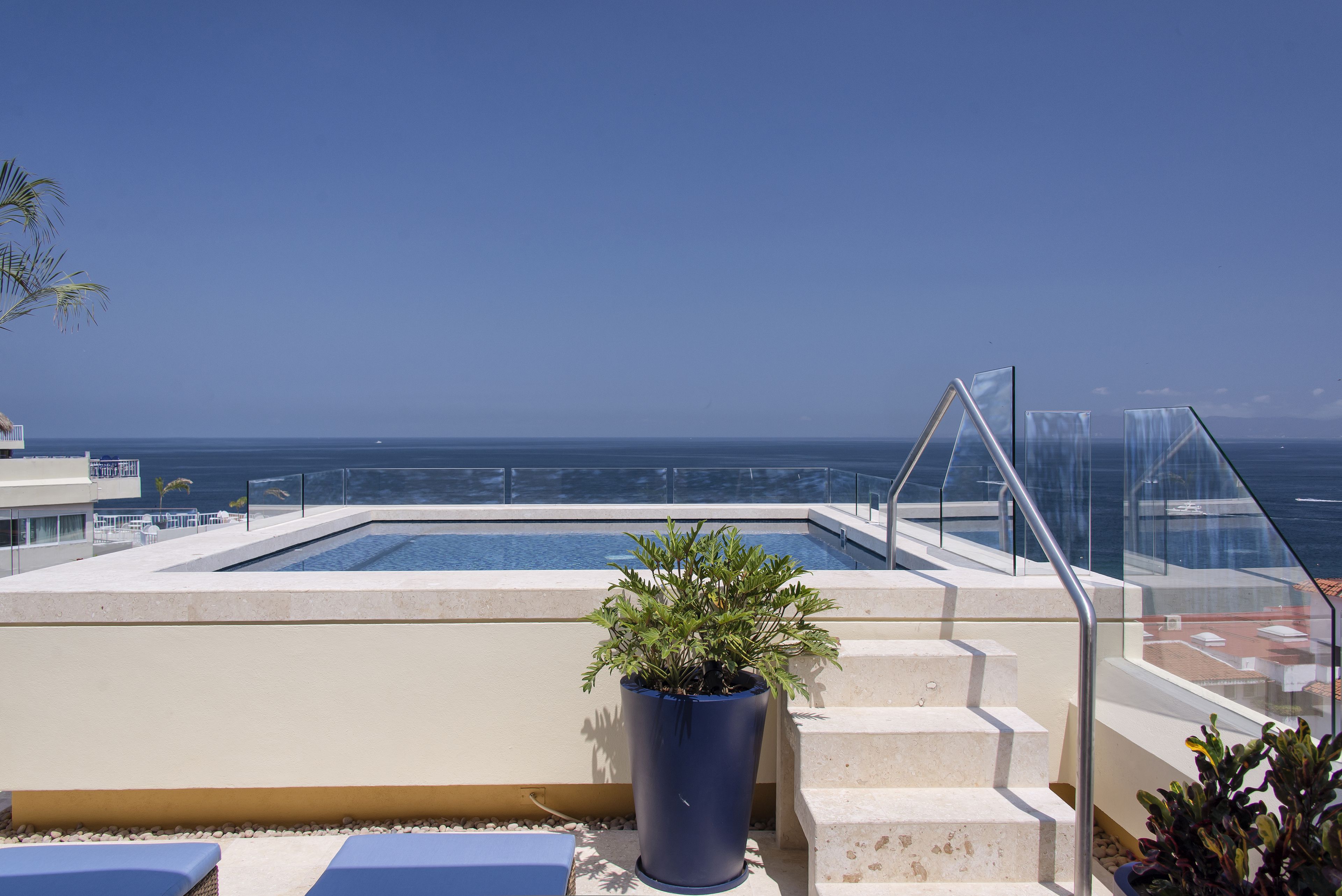 Ein Poolbereich auf dem Dach mit freiem Blick auf den Ozean, einer Topfpflanze und einer Treppe zum Pool.