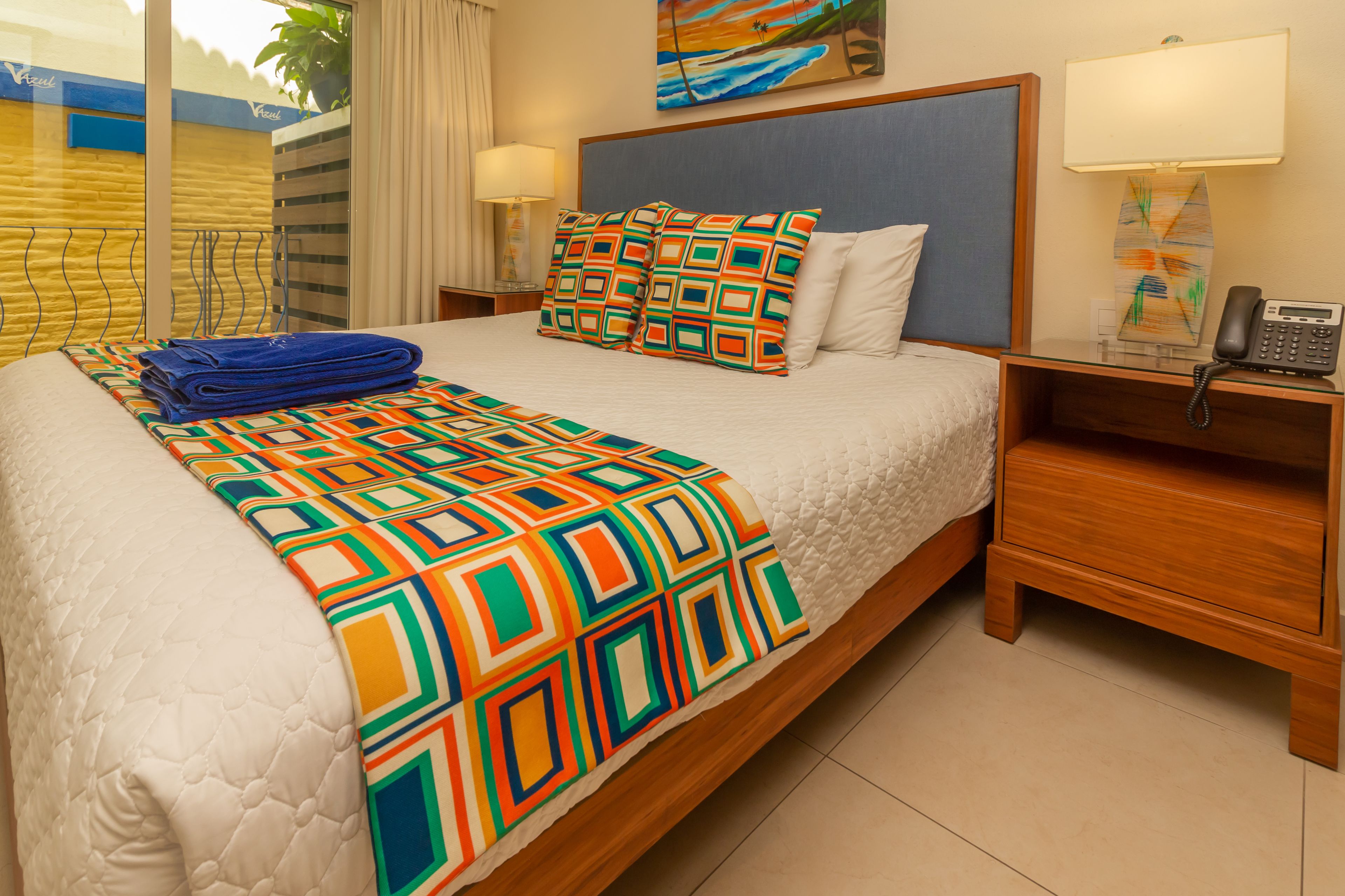 Una habitación de hotel con una cama grande, una mesita de noche con un teléfono y un cuadro en la pared.