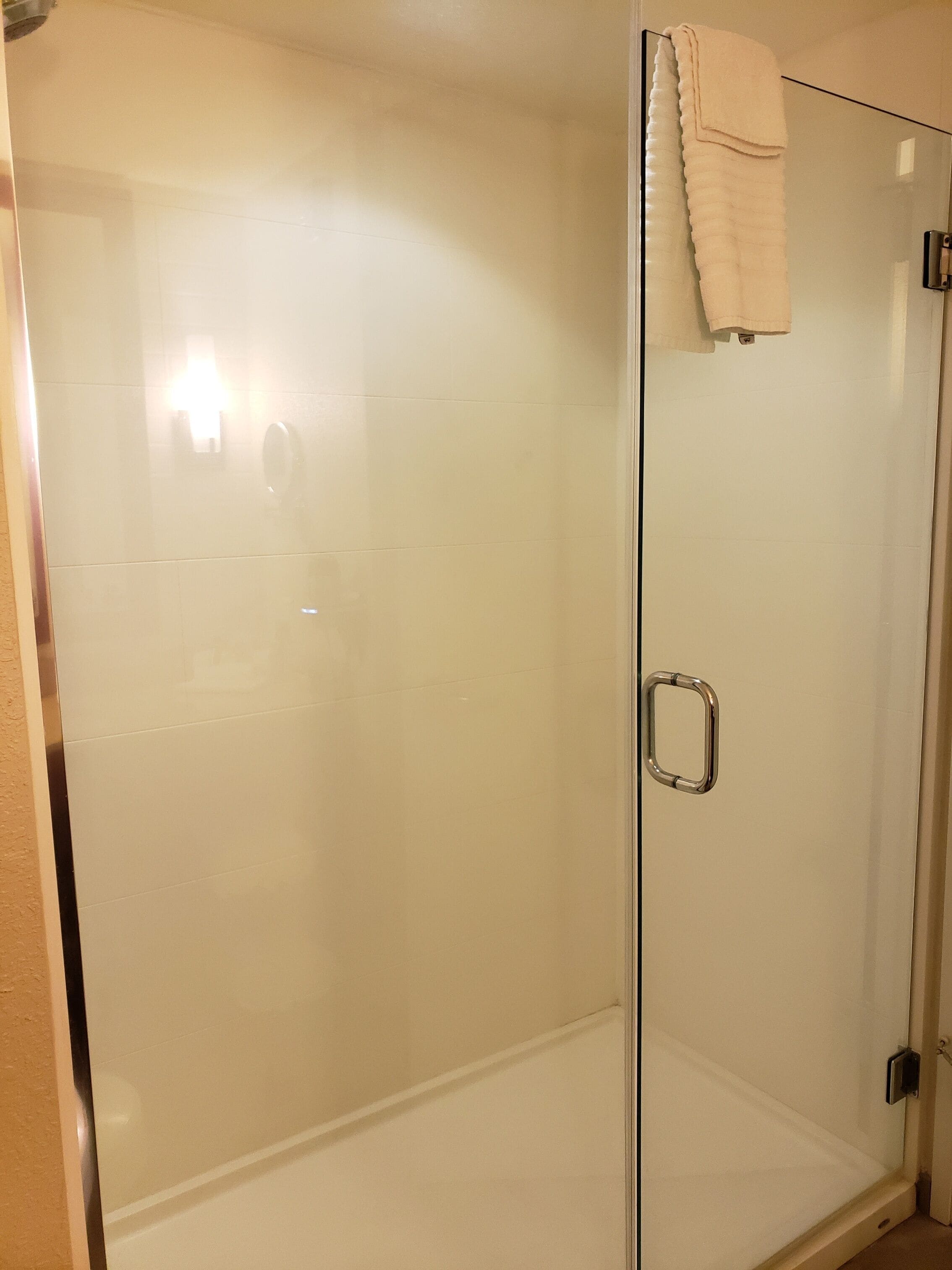 Una ducha con mampara de vidrio, pared de azulejos blancos y una toalla colgada en la puerta.