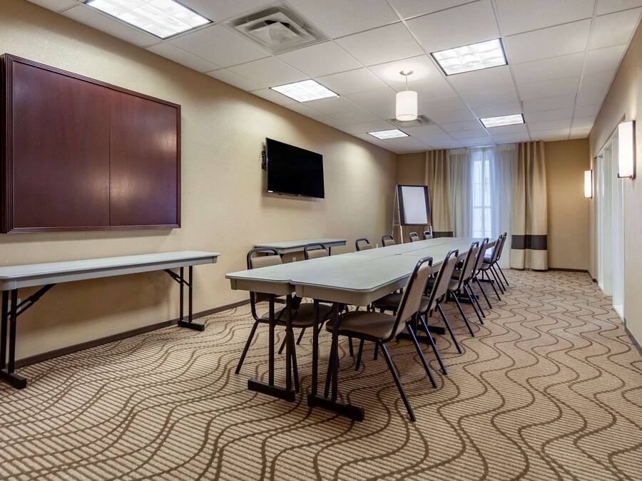 Un salón de conferencias con una larga mesa, sillas, una pantalla de proyector y una televisión.