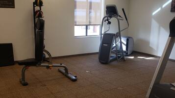 A fitness room with exercise equipment, a window, and a carpeted floor.