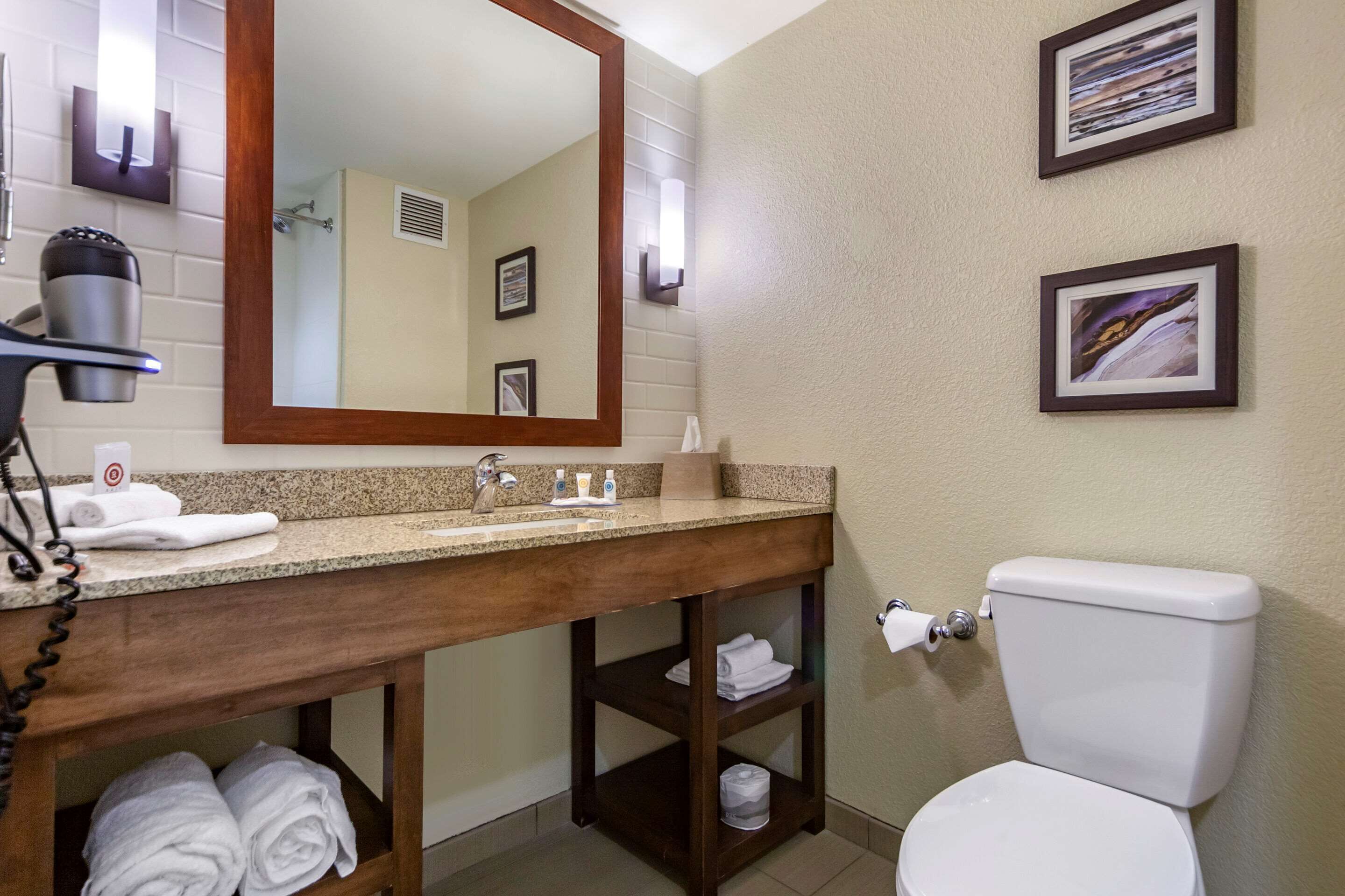 A bathroom with a wooden vanity, a sink, a toilet, and two framed pictures on the wall.