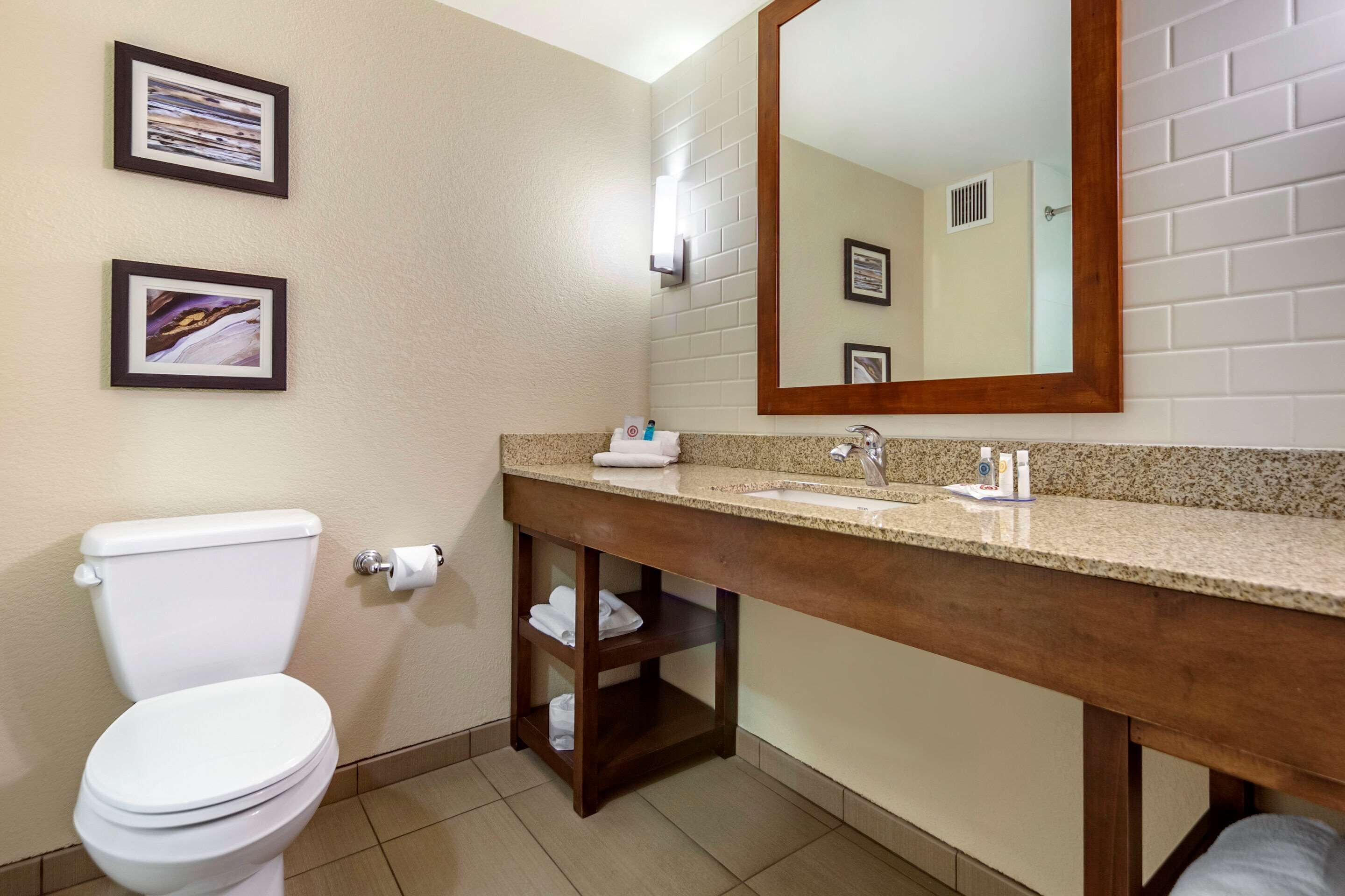 A bathroom with a toilet, sink, and mirror. There are framed pictures on the wall and a towel rack below the sink.