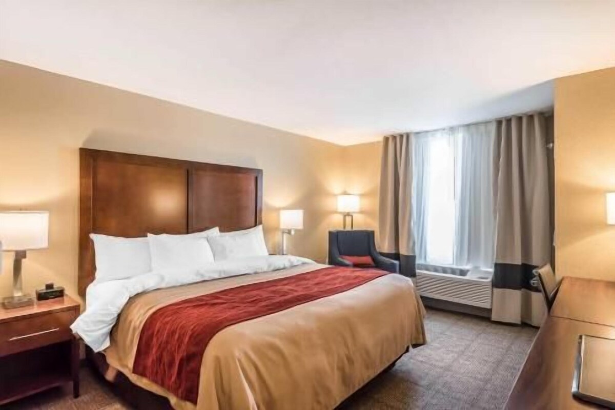A hotel room with a bed, bedside tables, a chair, and a window with curtains.