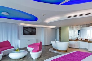 Ein modernes Hotelzimmer mit gewölbter Decke, einem großen Flachbildfernseher, einer weißen Badewanne und einer rosa-weißen Sofagarnitur.