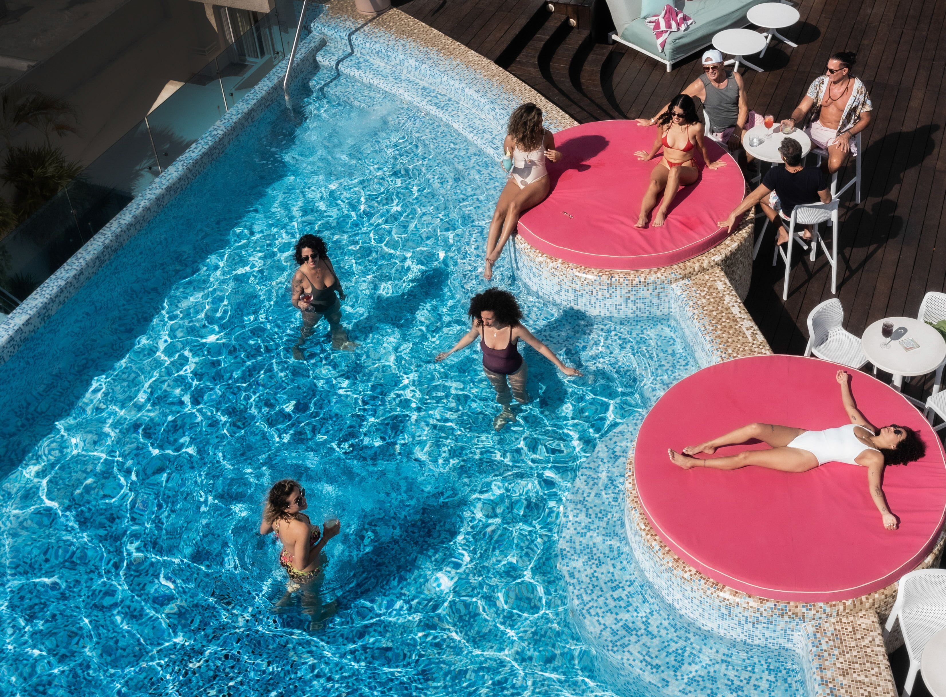 A swimming pool with multiple sun loungers and a deck area with tables and chairs.