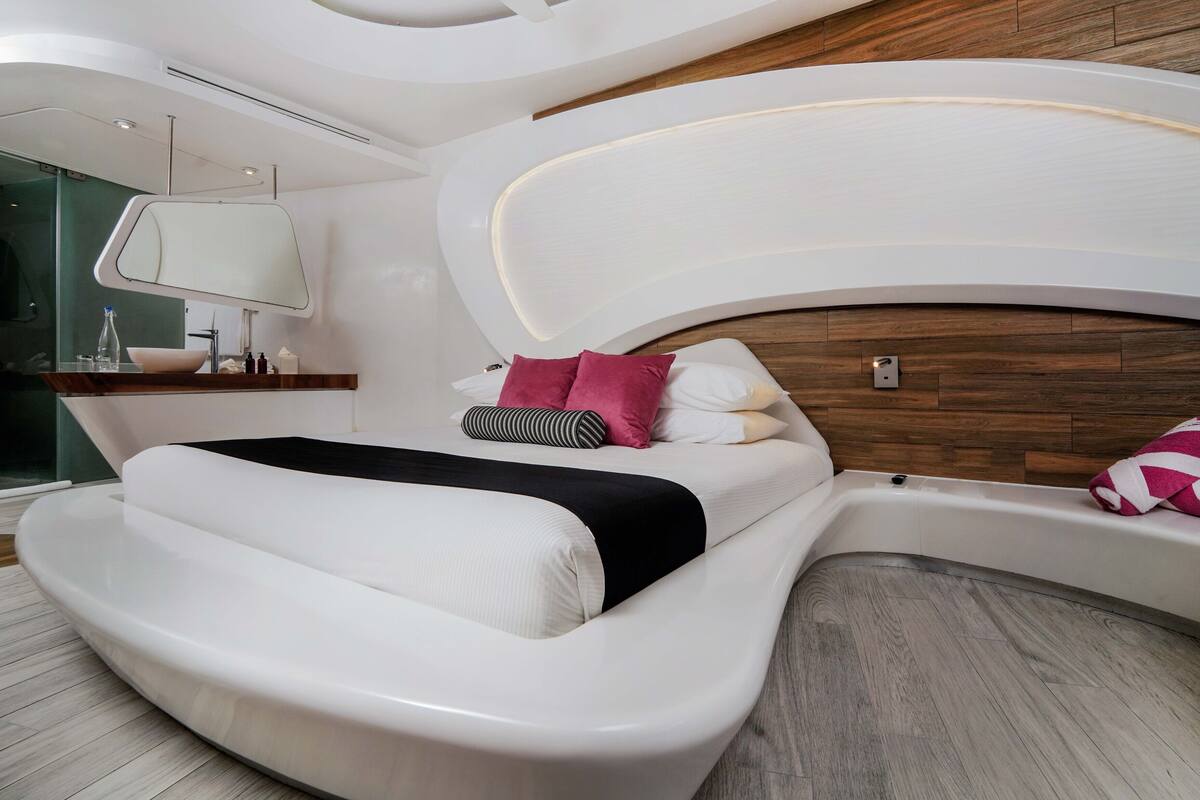 Ein modernes Schlafzimmer mit einem gebogenen Bett, einem Holzkopfbrett, einem Nachttisch mit Spiegel und einer integrierten Badewanne.