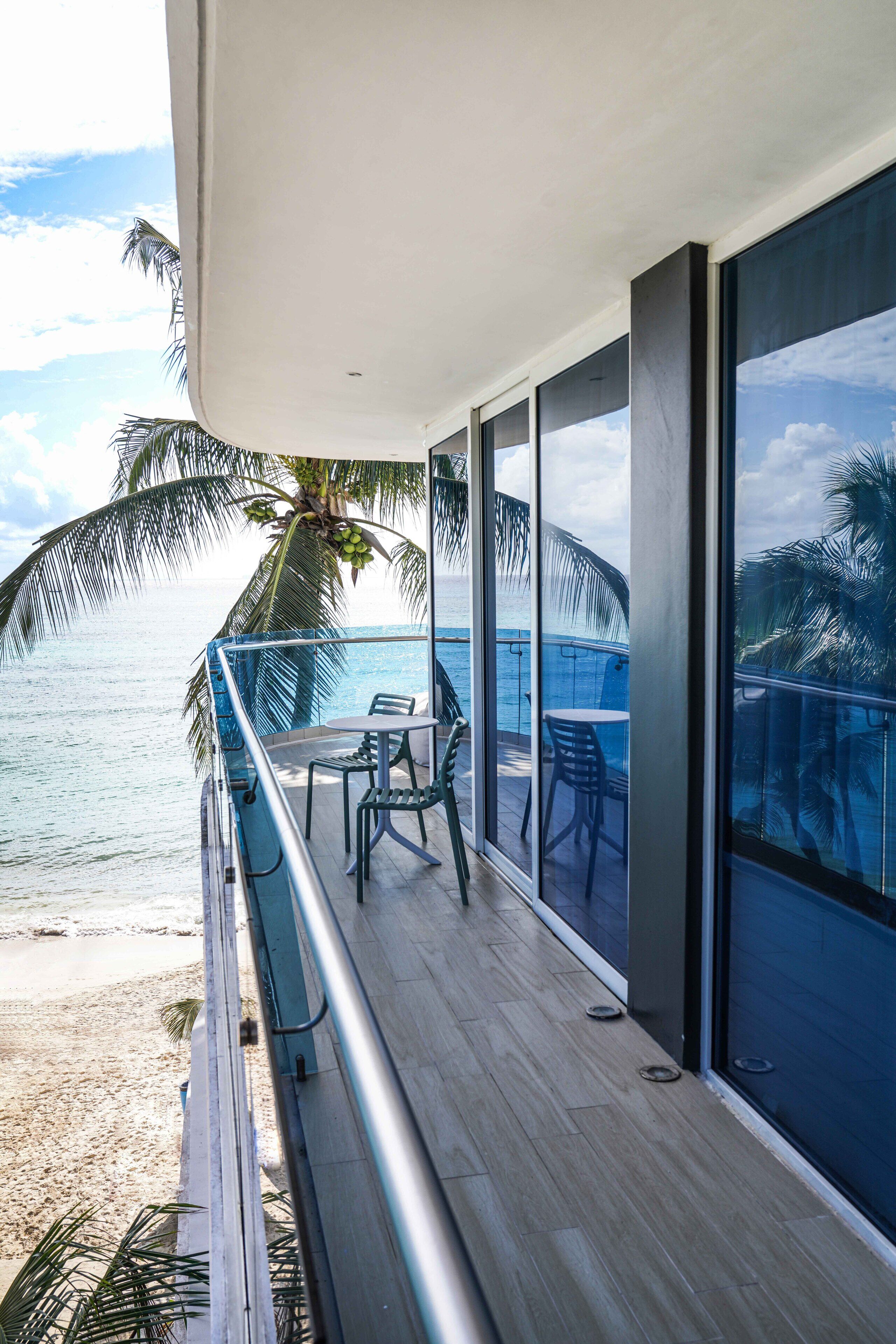 A balcony with a view of the ocean, a palm tree, and a table with chairs.