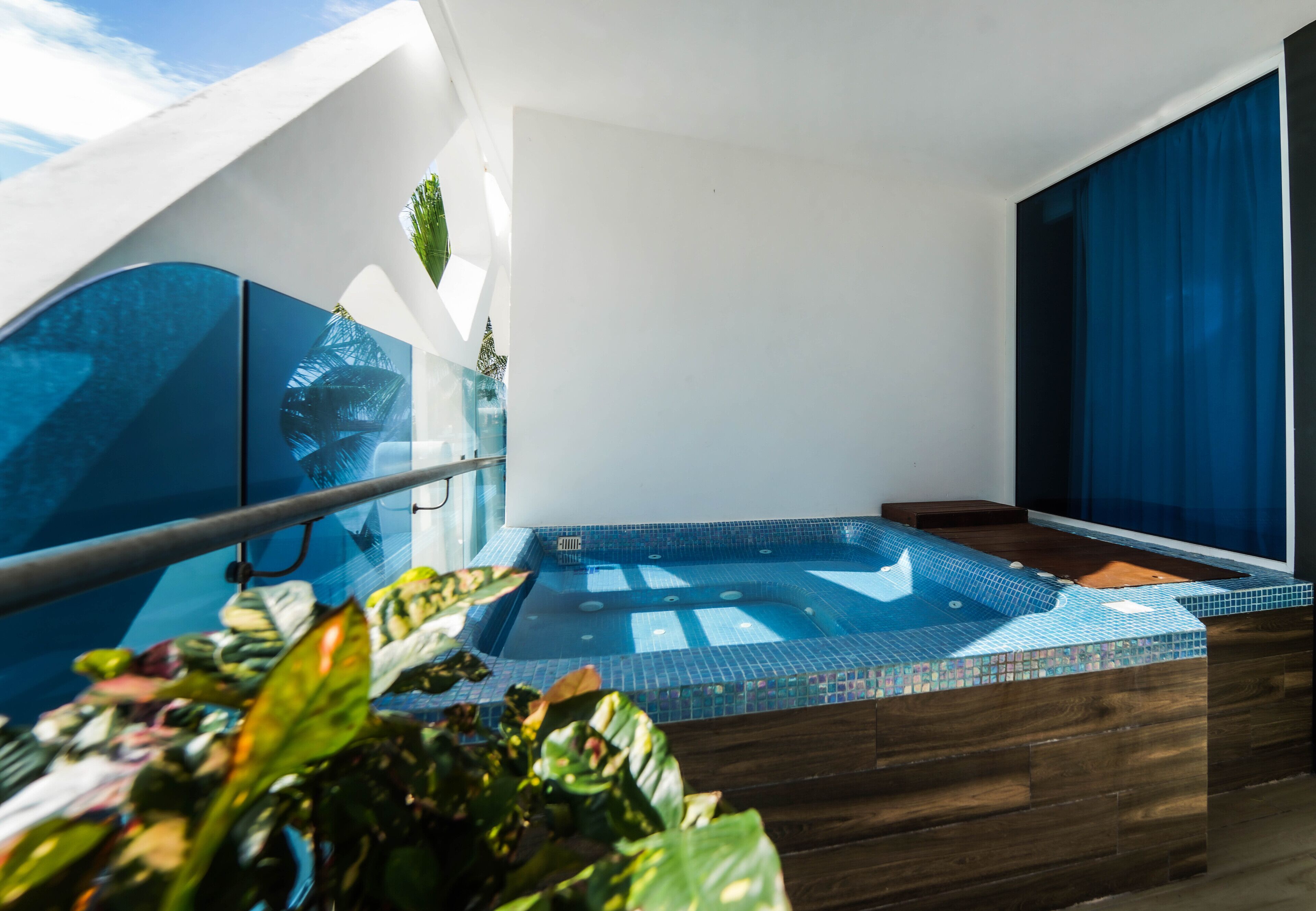 Un balcon moderne doté d’une balustrade en verre, d’un jacuzzi et d’une végétation luxuriante.