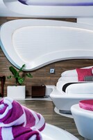 A modern spa room with a curved white bathtub, a wooden floor, a white sofa, and a potted plant.