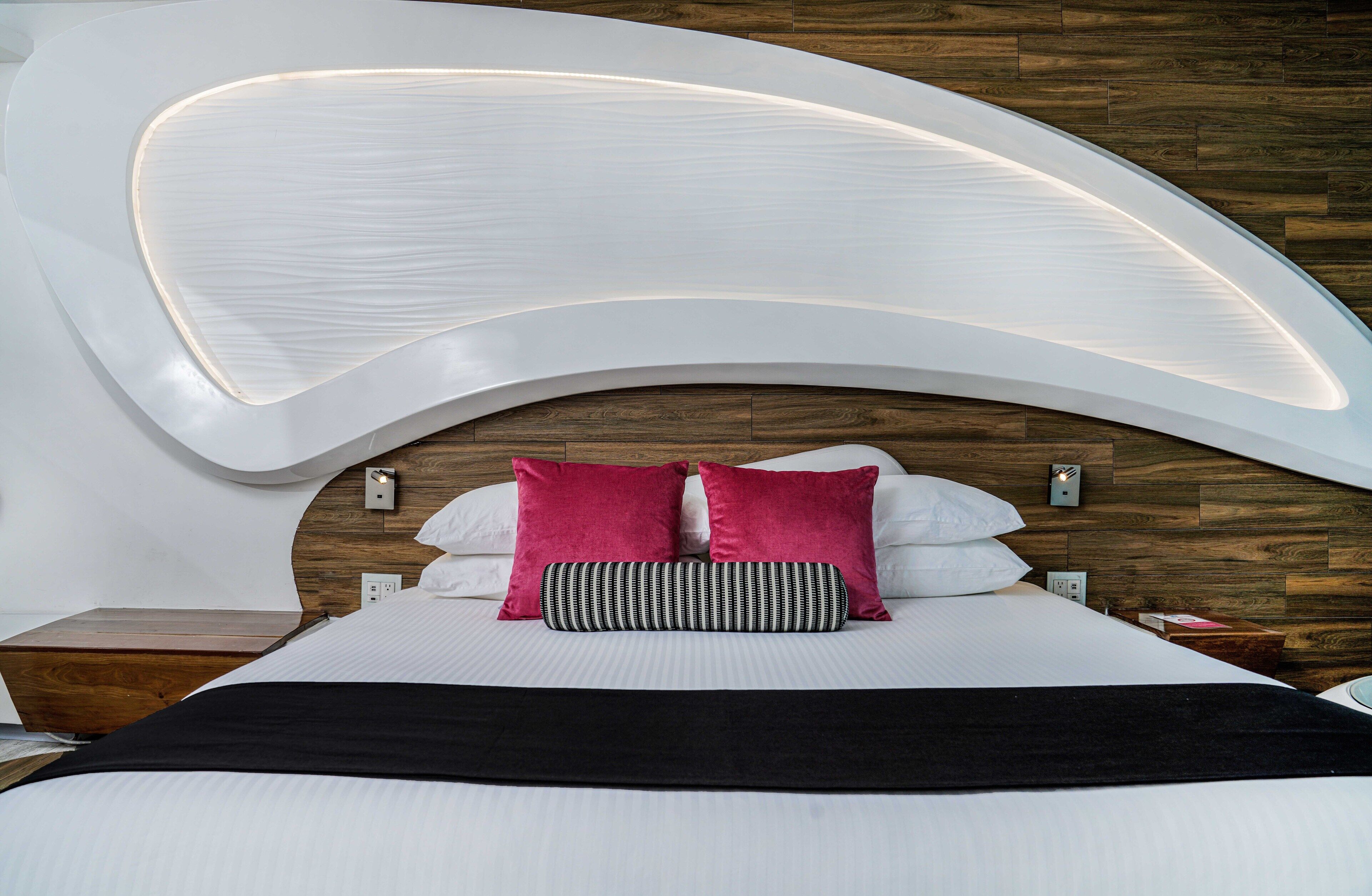 A modern bedroom with a curved ceiling, a wooden headboard, and a black and white striped pillow.