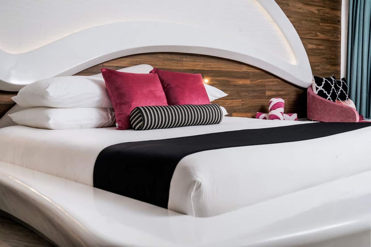 Ein modernes Bett mit einer geschwungenen Kopfteil, weißer Bettwäsche und mehreren Kissen in verschiedenen Farben und Mustern.