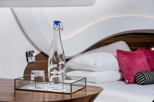 Una habitación de hotel moderna con una mesita de madera, una botella de vidrio transparente y dos vasos sobre una bandeja.