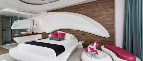 A modern bedroom with a curved ceiling, a large bed with white bedding and pink pillows, a bedside table, and a built-in bench with a pink cushion.
