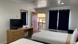 A hotel room with a bed, a desk with a TV, a phone, and a window with curtains. - Palms Inn & Suites (Palmdale)