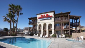 A hotel with a pool, outdoor seating, and palm trees. - Palms Inn & Suites (Palmdale)