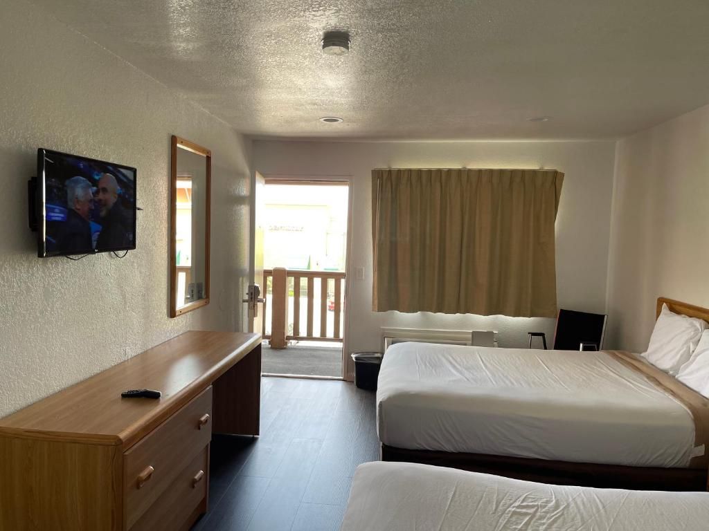 Ein Hotelzimmer mit zwei Betten, einem Fernseher, einem Schreibtisch und einem Fenster mit Vorhängen.