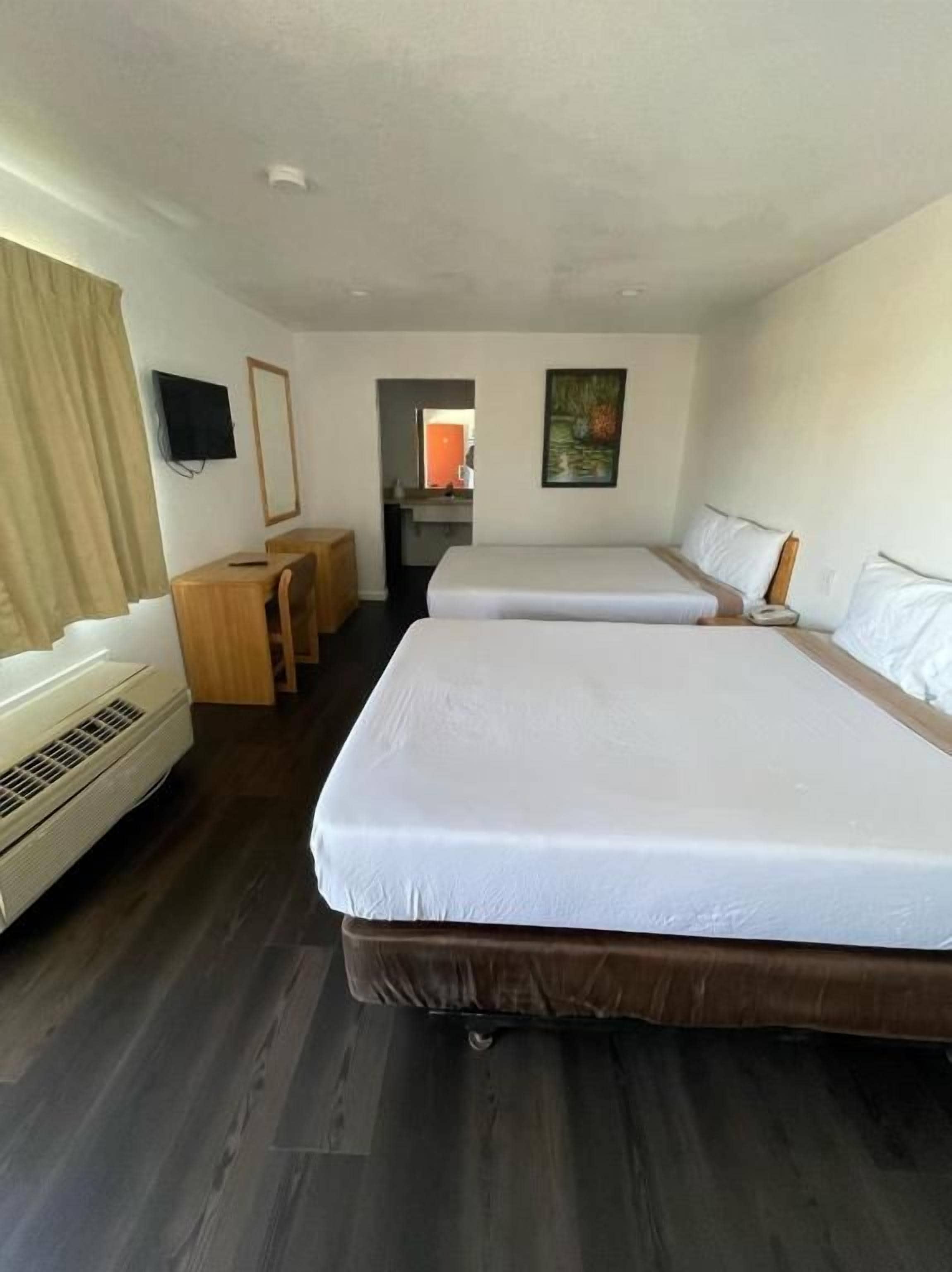 Habitación de hotel con dos camas, un escritorio, una silla, un televisor y un cuadro en la pared.