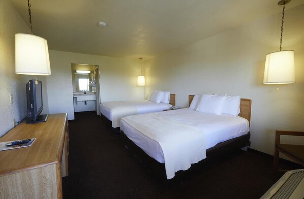 A hotel room with two beds, a desk with a television, a mirror, and two bedside lamps.