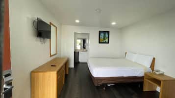 A hotel room with a bed, a desk, a TV, and a painting on the wall.