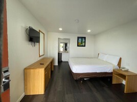A hotel room with a bed, a desk, a TV, and a painting on the wall.