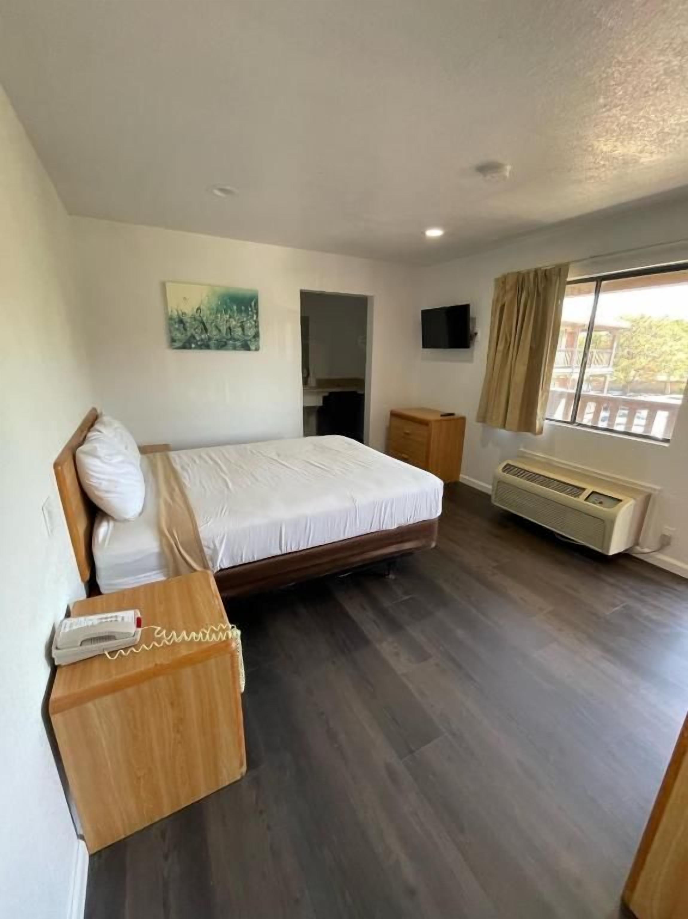 Un dormitorio con cama, mesita de noche y ventana con cortinas.