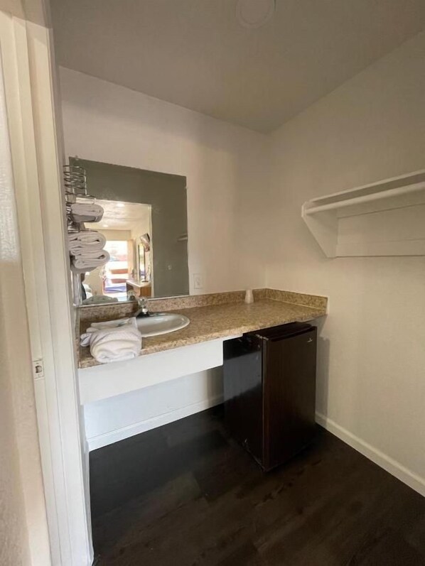 A bathroom with a sink, mirror, towel rack, and dark flooring. - Palms Inn & Suites (Palmdale)