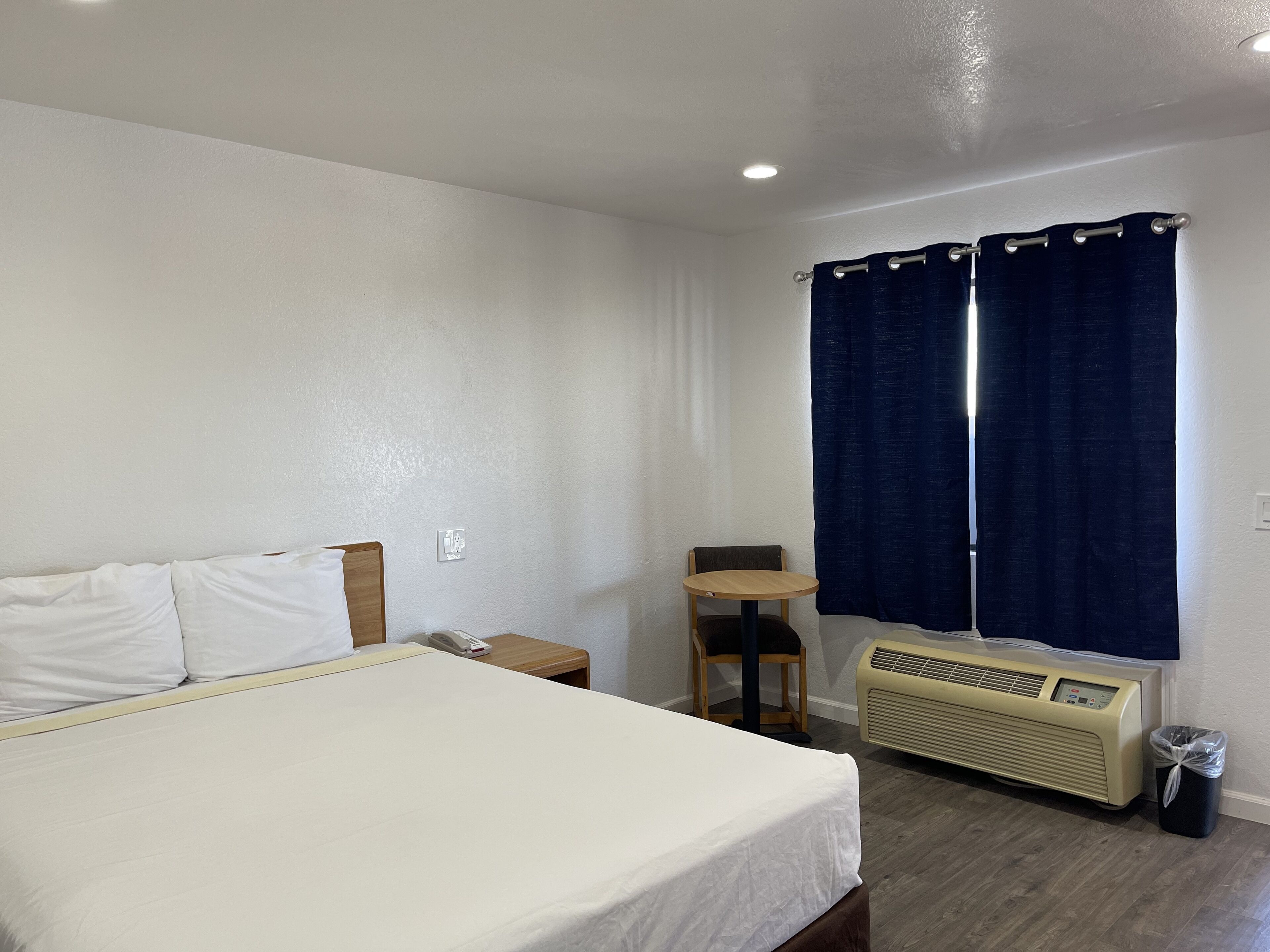 A hotel room with a bed, a small table, a chair, a heater, and a window with curtains.