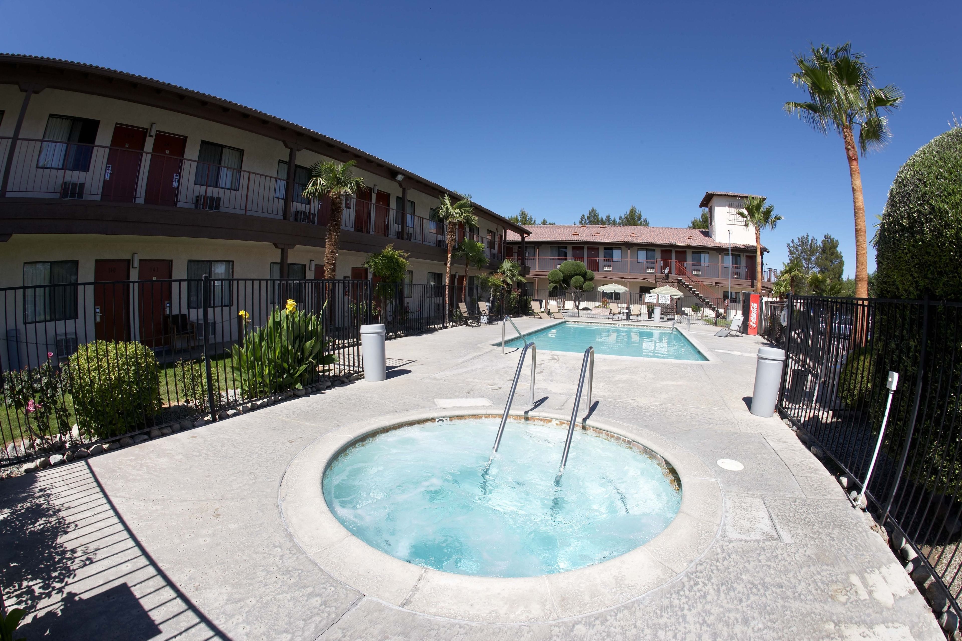 A hotel with a swimming pool, outdoor seating, and palm trees.
