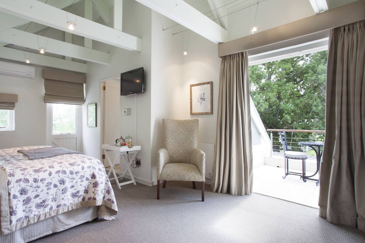Una habitación de hotel con cama, una silla, un escritorio, televisor y un balcón con mesa y sillas.
