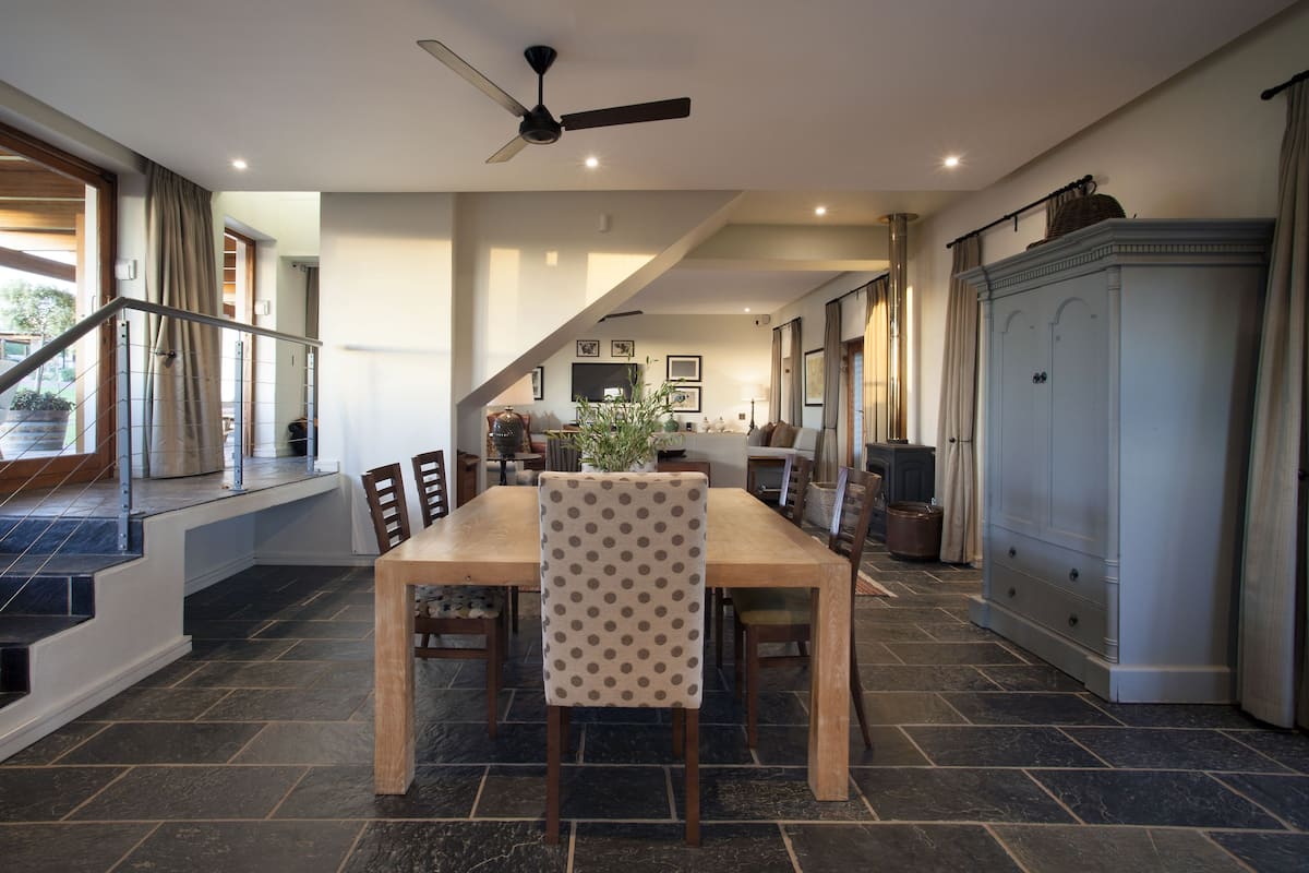 Un comedor amplio con una mesa y sillas de madera, un ventilador de techo y una escalera que conduce a un nivel superior.