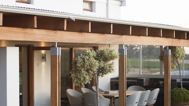Een modern huis met een overdekte patio, compleet met een eettafel en stoelen, omringd door potplanten.