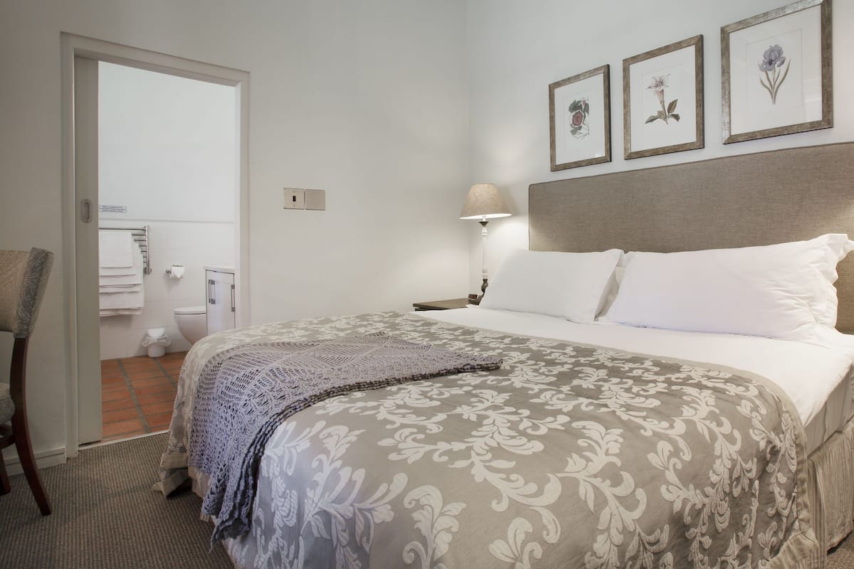 Habitación de hotel ordenada con una cama, dos lámparas de noche, un cabecero y tres cuadros con flores en la pared.
