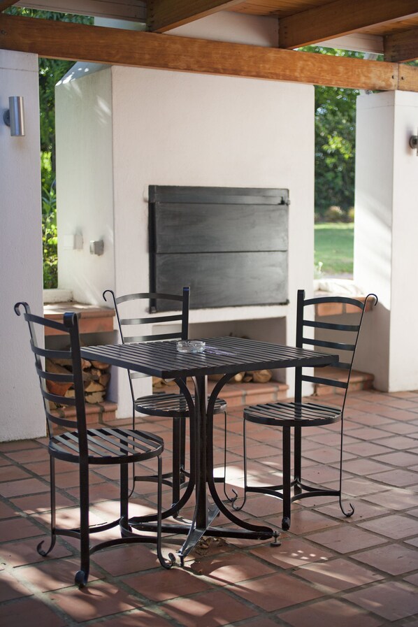 A patio with a metal table and chairs, a grill, and a white wall with a window. - Klein Welmoed Luxury Guest House (Stellenbosch)