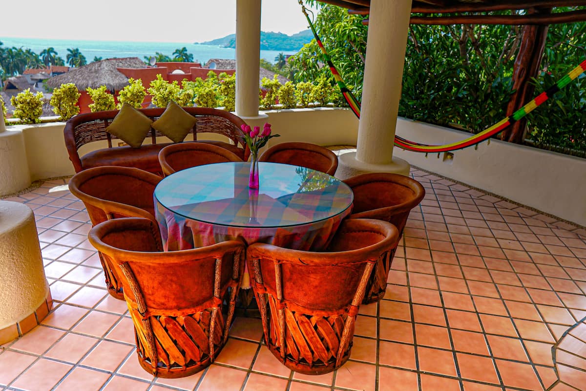 Una mesa redonda de cristal con sillas de terracota, un florero con flores y vista al océano.