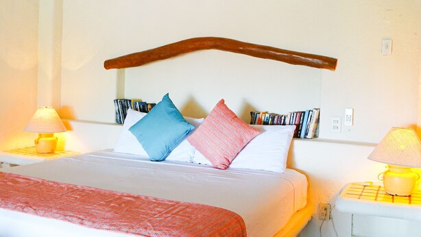 Ein Schlafzimmer mit Bett, Kissen, Nachttisch, Lampe, Wandklimaanlage und Bücherregal.