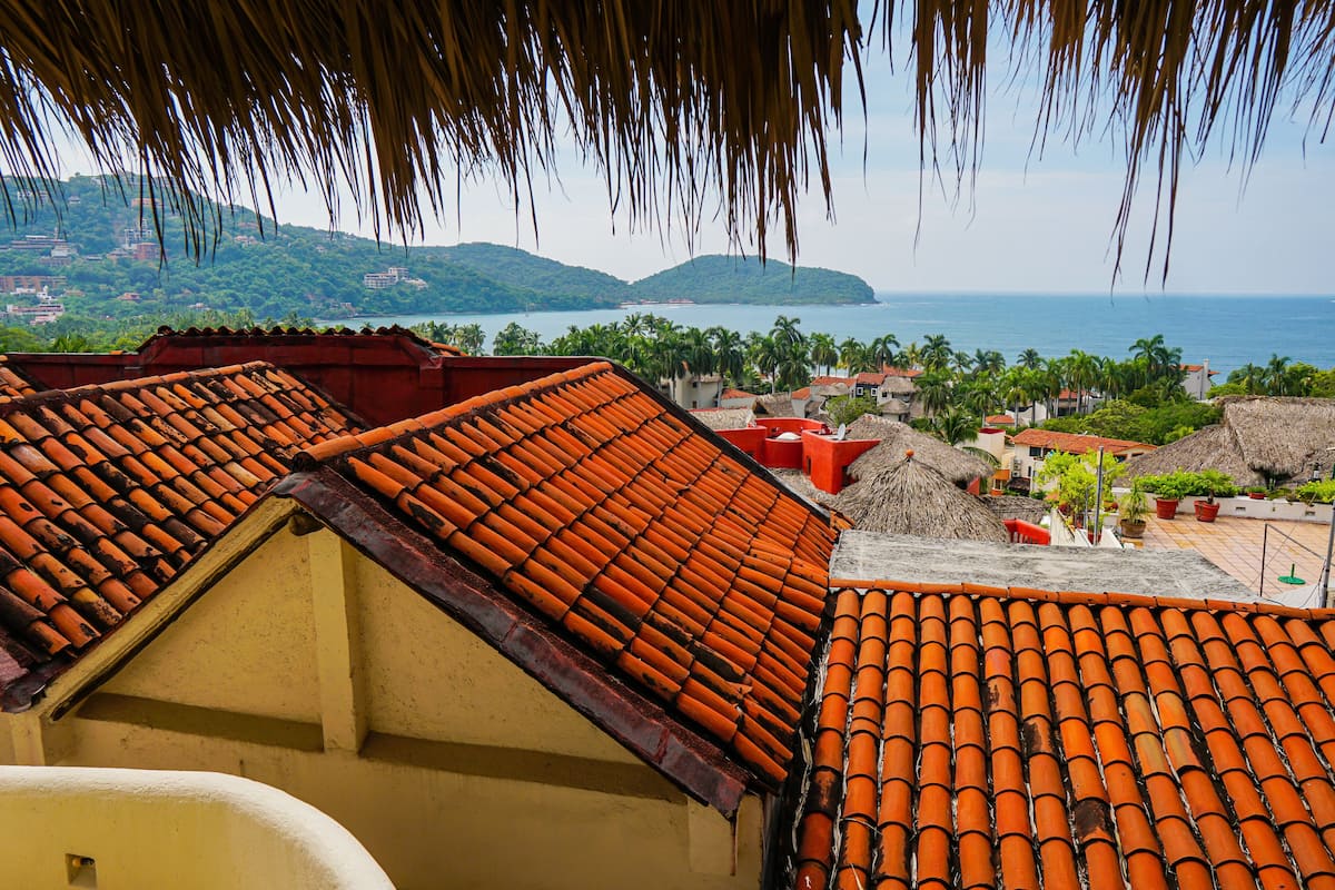 Vista costera con tejados de terracota y una imagen despejada del mar y las colinas al fondo.