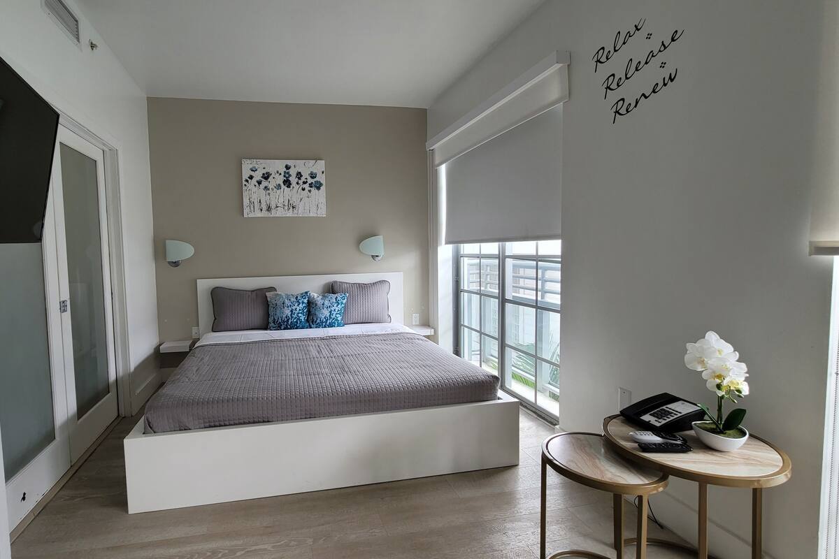 Une chambre à coucher comprenant un lit, des tables de chevet, une œuvre d’art accrochée au mur et une fenêtre donnant sur un paysage.