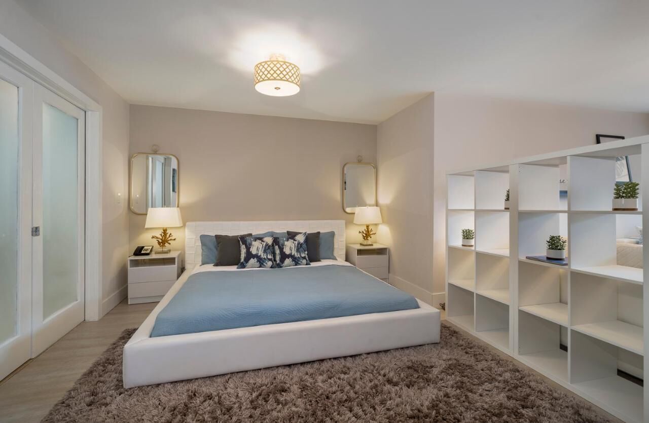 A bedroom with a large bed, two bedside tables with lamps, a wardrobe, and a ceiling light fixture.
