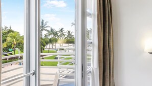 A balcony with a view of a well-maintained lawn, palm trees, and a distant building. - Strand Ocean Drive Suites (Miami Beach)