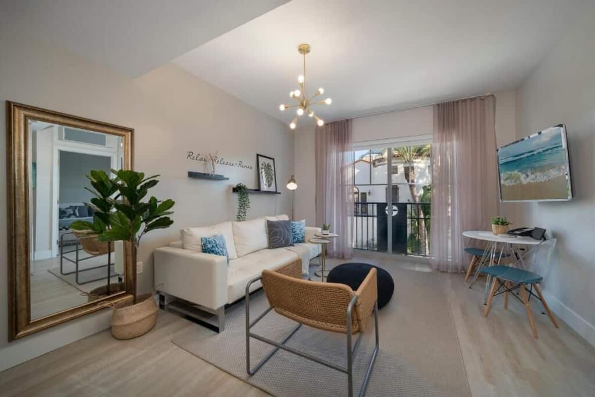 Un salon moderne avec un canapé, un grand miroir, un luminaire suspendu et une vue sur l’extérieur par une fenêtre.