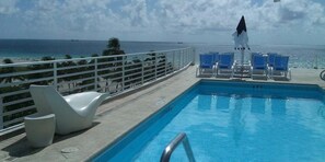 A pool with a view of the ocean, lounge chairs, and a white umbrella. - Strand Ocean Drive Suites (Miami Beach)