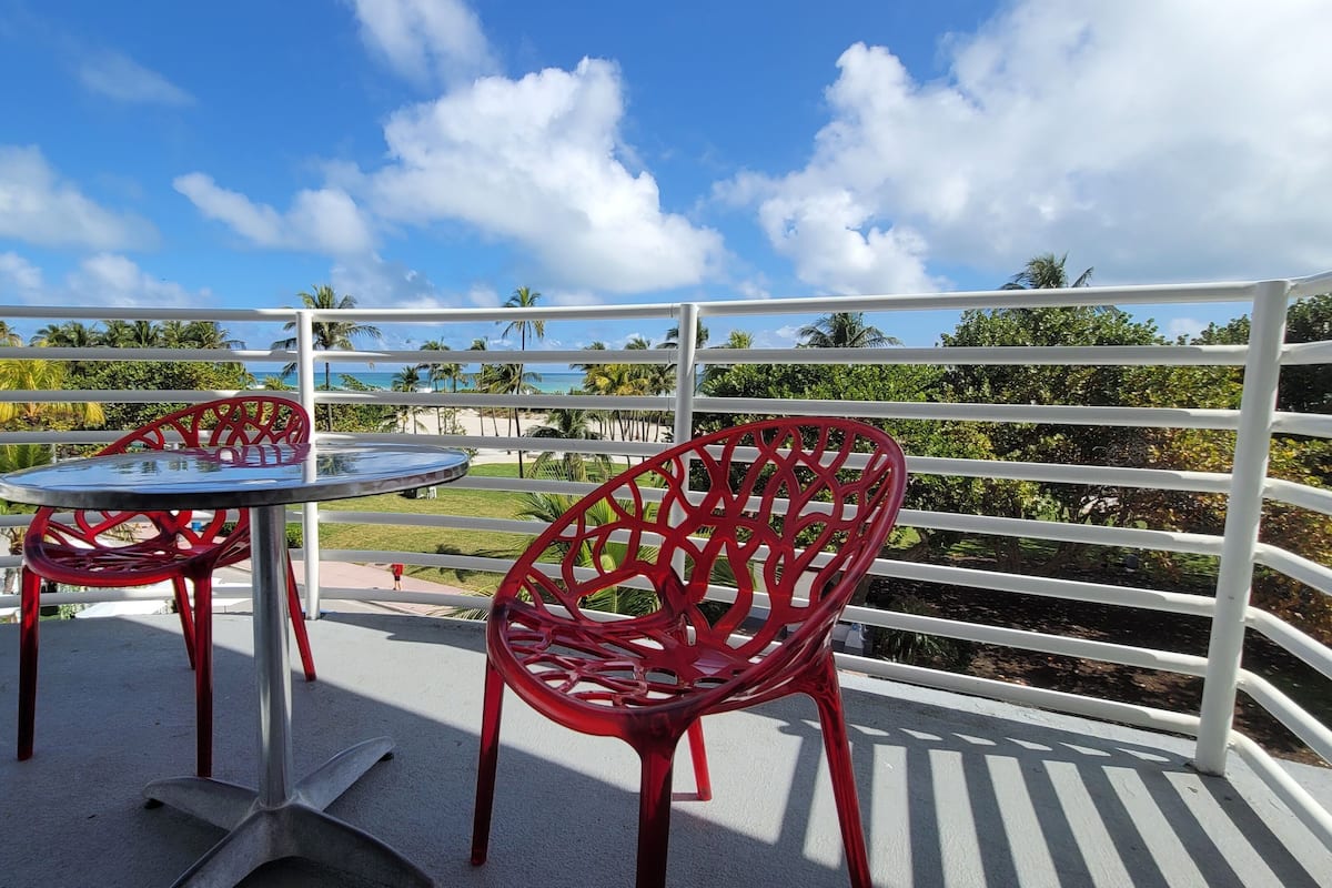 Un balcon avec une table et deux chaises, donnant sur une plage et des palmiers.