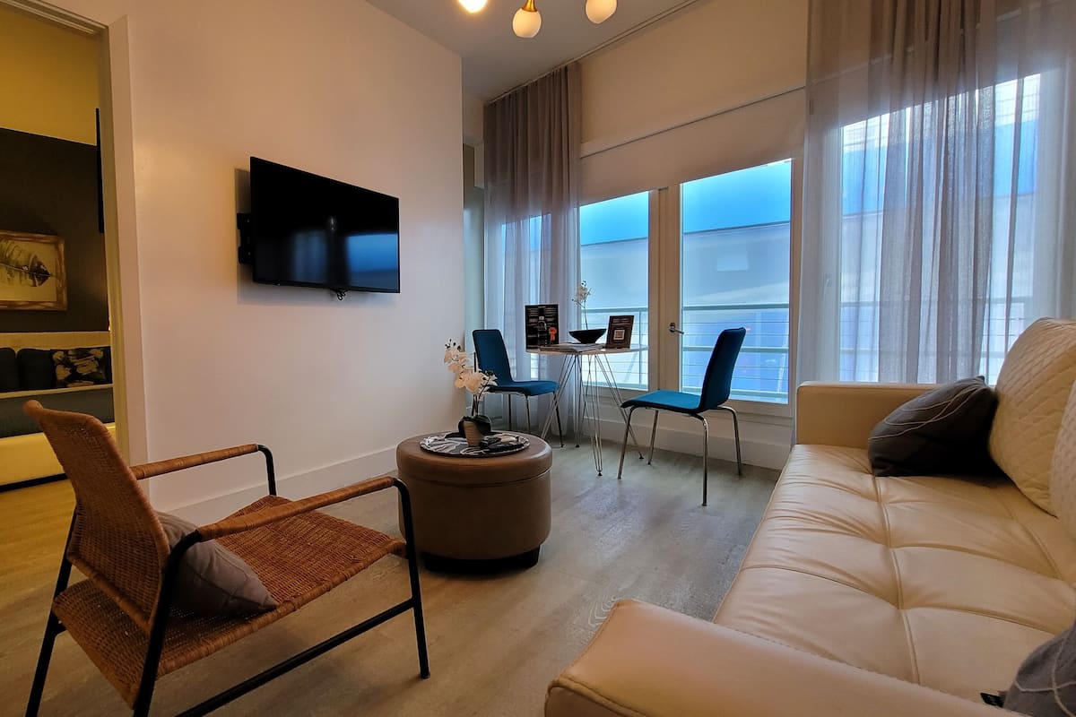 Un salon moderne avec un téléviseur à écran plat, un canapé, un fauteuil et une petite table sur laquelle est posé un vase de fleurs.